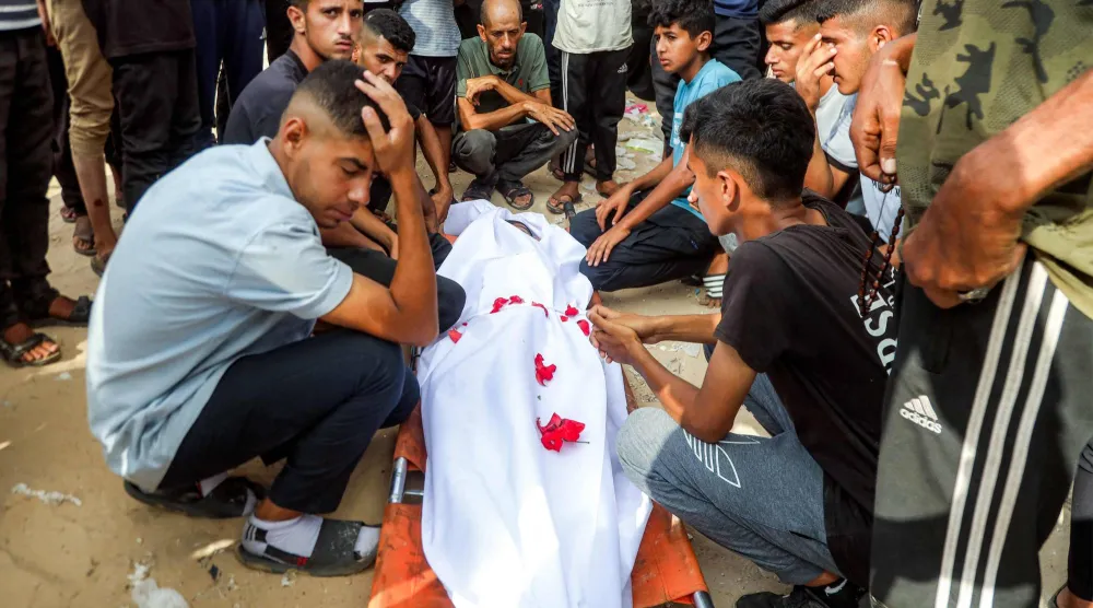 فلسطينيون يجلسون بجانب إحدى ضحايا القصف الإسرائيلي الليلي على مخيم للنازحين في منطقة المواصي بخان يونس (أ.ف.ب)