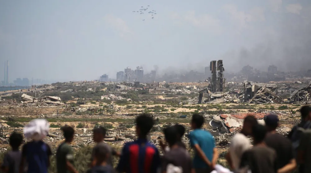 Palestinians watch aid pallets parachute down after being dropped from a military plane over Nuseirat in the central Gaza Strip during an airdrop mission above the Israel-besieged Palestinian territory on August 5, 2025. (Photo by Eyad BABA / AFP)