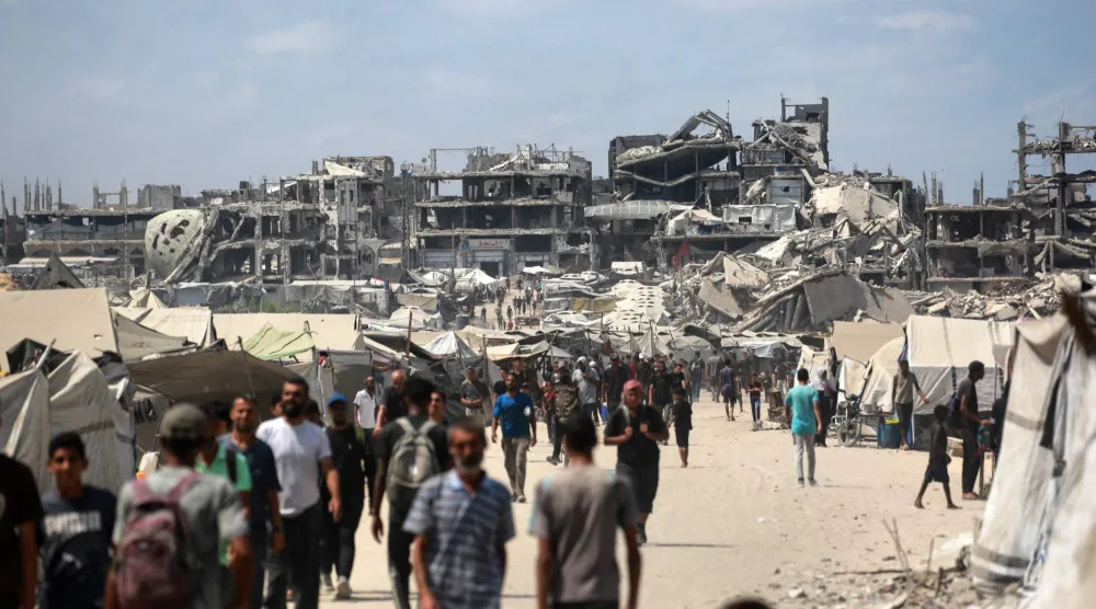 فلسطينيون يسيرون في شارع بالقرب من المباني المتضررة جراء الحرب في مدينة غزة (أ.ف.ب)