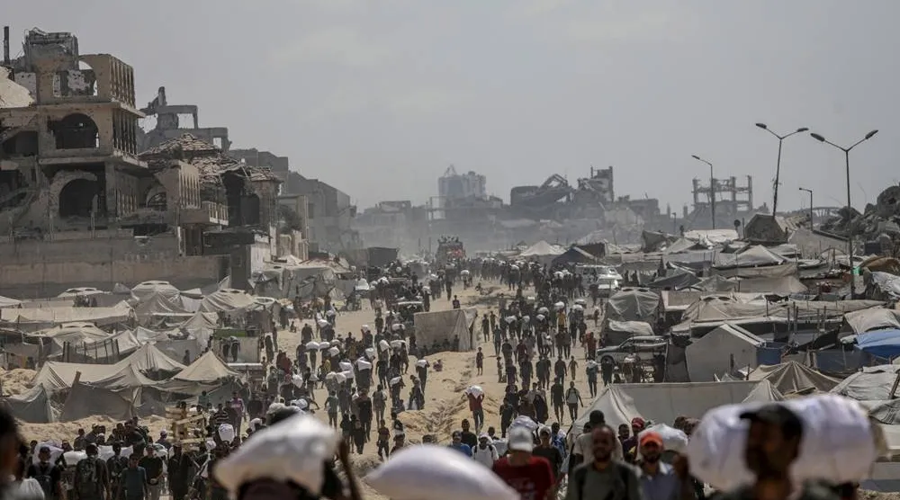 Internally displaced Palestinians carry bags of flour near a food distribution point in Zikim, northern Gaza Strip, 08 August 2025. (EPA)