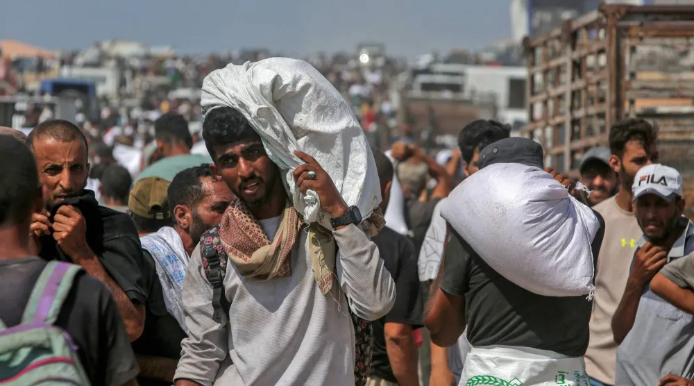نازحون فلسطينيون يحملون أجولة طحين بعد توقيفهم شاحنات تحمل مساعدات في خان يونس جنوب قطاع غزة (أ.ف.ب)