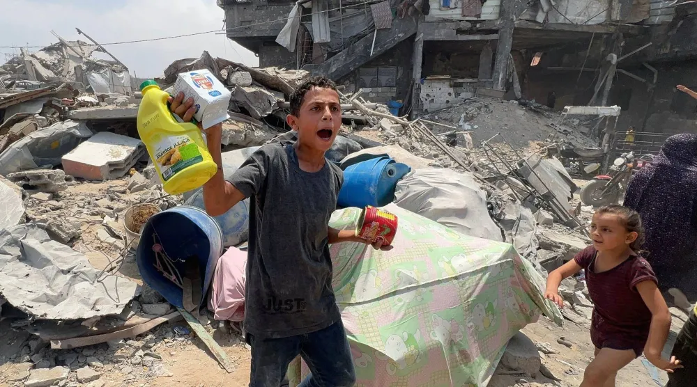 فتى فلسطيني يحمل مواد غذائية استطاع الحصول عليها من حزمة مساعدات أسقطت جوا في جباليا شمال قطاع غزة أمس (أ.ف.ب)