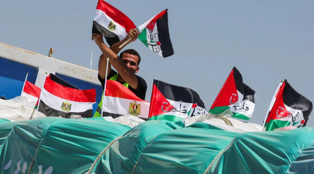 شخص يحمل العلمين المصري والفلسطيني على شاحنة تحمل مساعدات إنسانية بالقرب من معبر رفح (رويترز)