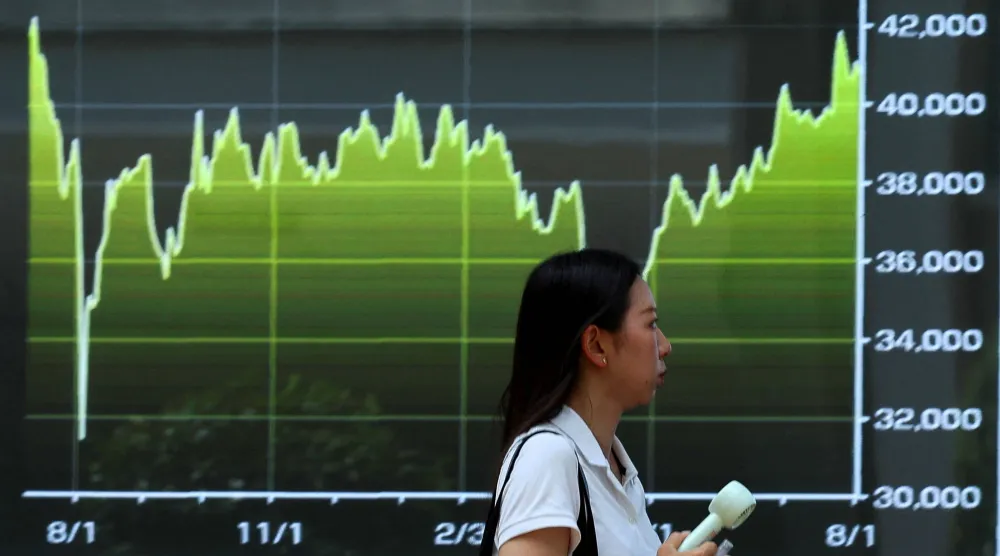 امرأة تسير بجانب شاشة تعرض رسماً بيانياً لتحركات مؤشر «نيكي» للأسهم اليابانية (رويترز)