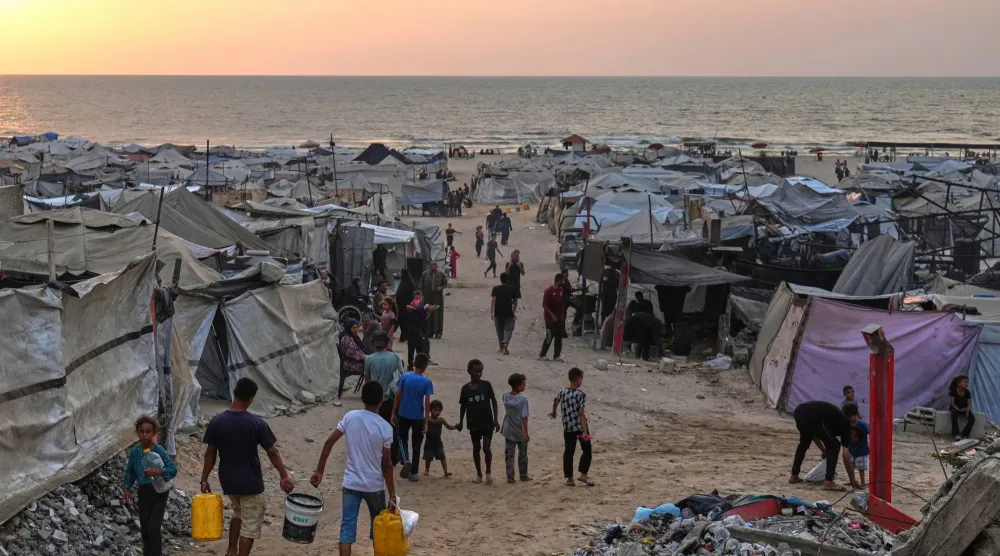 نازحون فلسطينيون يسيرون في مخيم مؤقت على طول الشاطئ في مدينة غزة 10 أغسطس 2025 (أ.ب)