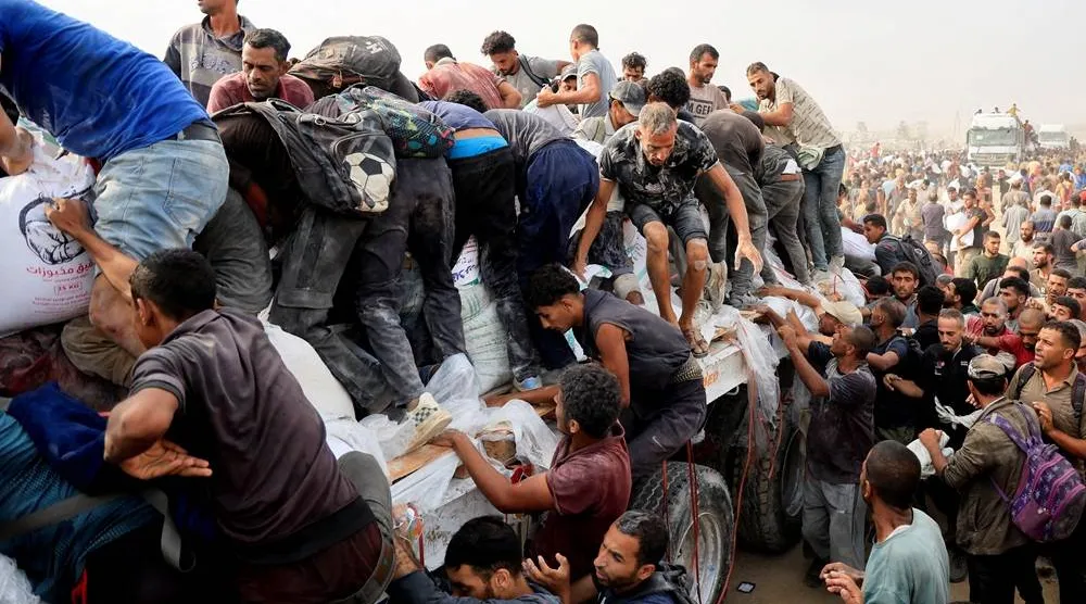  Palestinians scramble to collect aid supplies from trucks that entered through Israel, in Khan Younis, southern Gaza Strip, August 12, 2025. (Reuters)