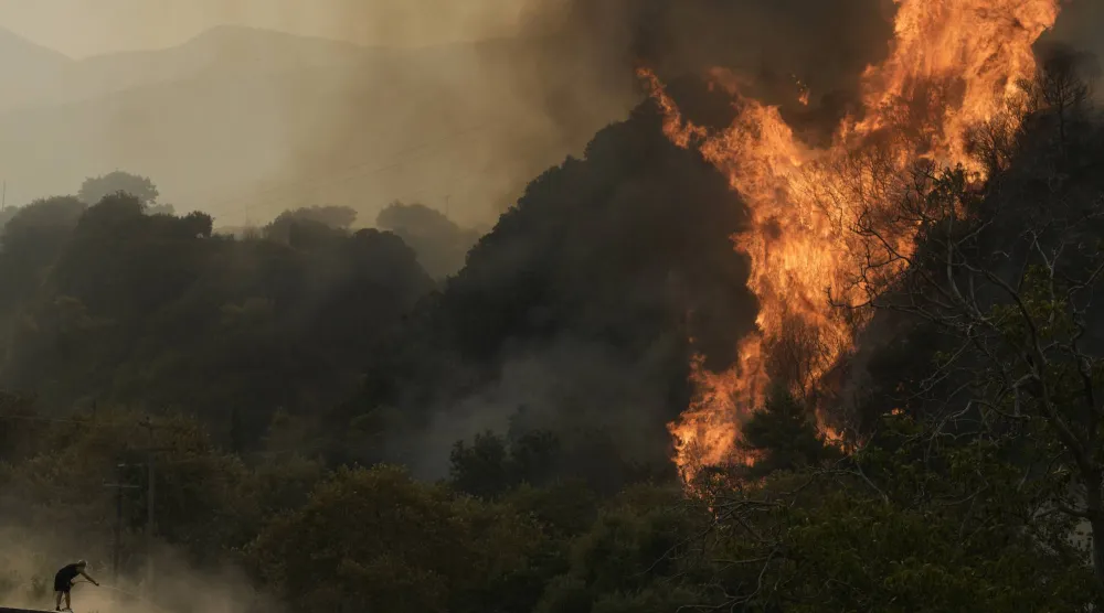 A man fights against a wildfire in Vounteni village, on the outskirts of Patras, western Greece, Wednesday, Aug. 13, 2025. (AP Photo/Thanassis Stavrakis)