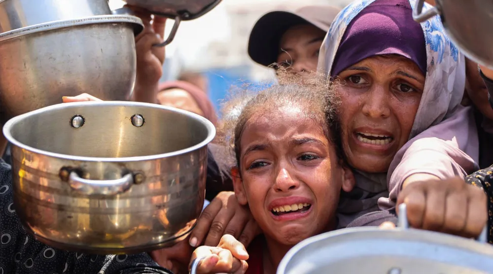 سيدة وطفلتها تبكيان خلال التدافع للحصول على قدر من الطعام المطبوخ وسط المجاعة في قطاع غزة (أ.ف.ب)
