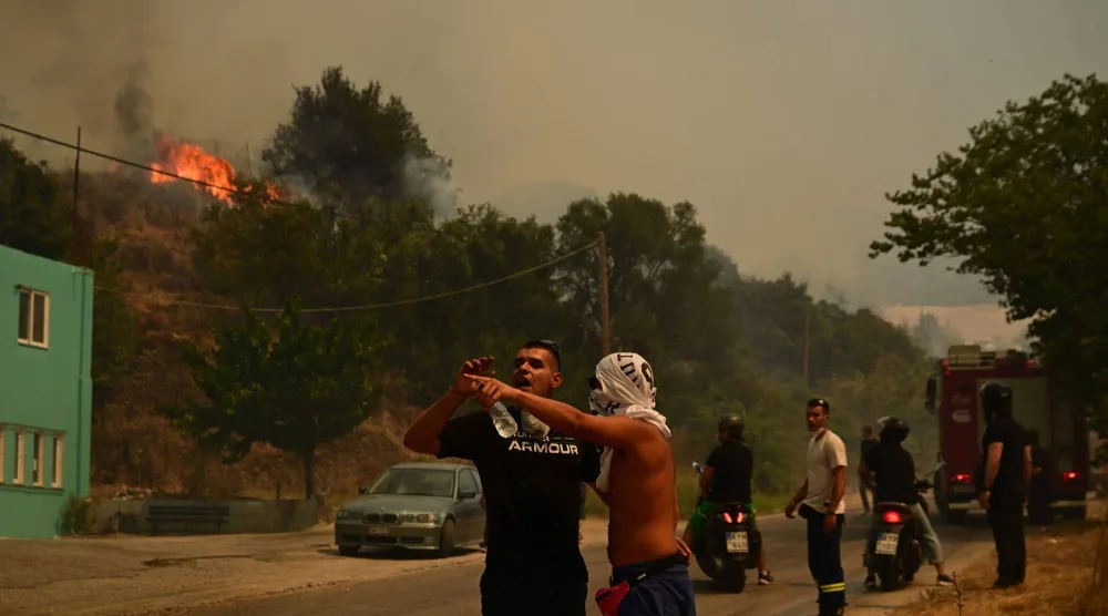 Local residents and firefighters stand along a road during efforts to extinguish a wildfire near the city of Patras, western Greece on August 13, 2025. (Photo by Aris MESSINIS / AFP)