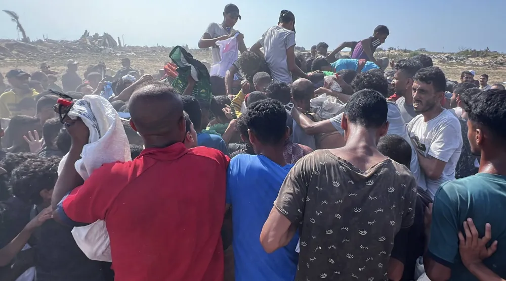 فلسطينيون يتجمعون حول حزمة مساعدات سقطت من الجو في النصيرات وسط قطاع غزة (د.ب.أ)