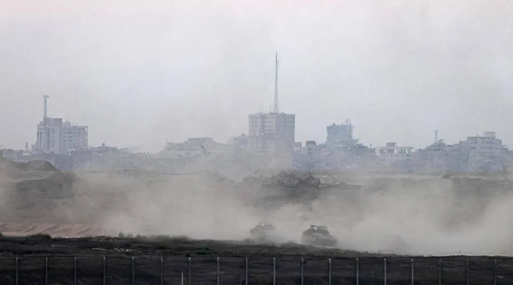  This picture taken from a position on the Israeli border with the Gaza Strip, shows Israeli armored personnel carriers driving behind the separation barrier on August 20, 2025. (AFP)