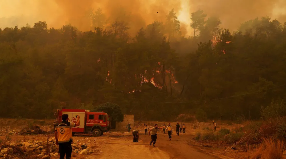 أفراد من الدفاع المدني السوري يكافحون حريقاً هائلاً في منطقة غابات بريف اللاذقية (رويترز)