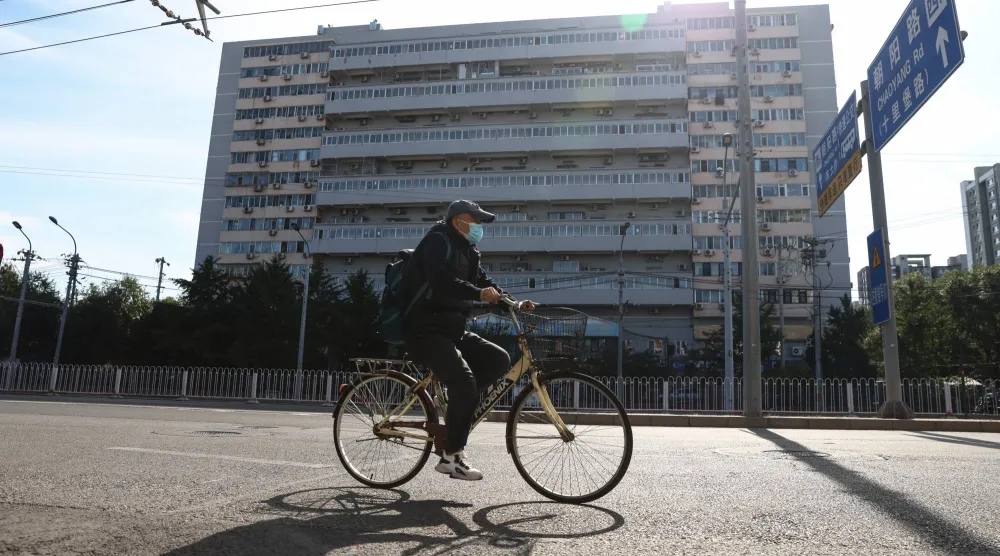 رجل مُسن يركب دراجة أمام مبنى سكني في بكين (إ.ب.أ)