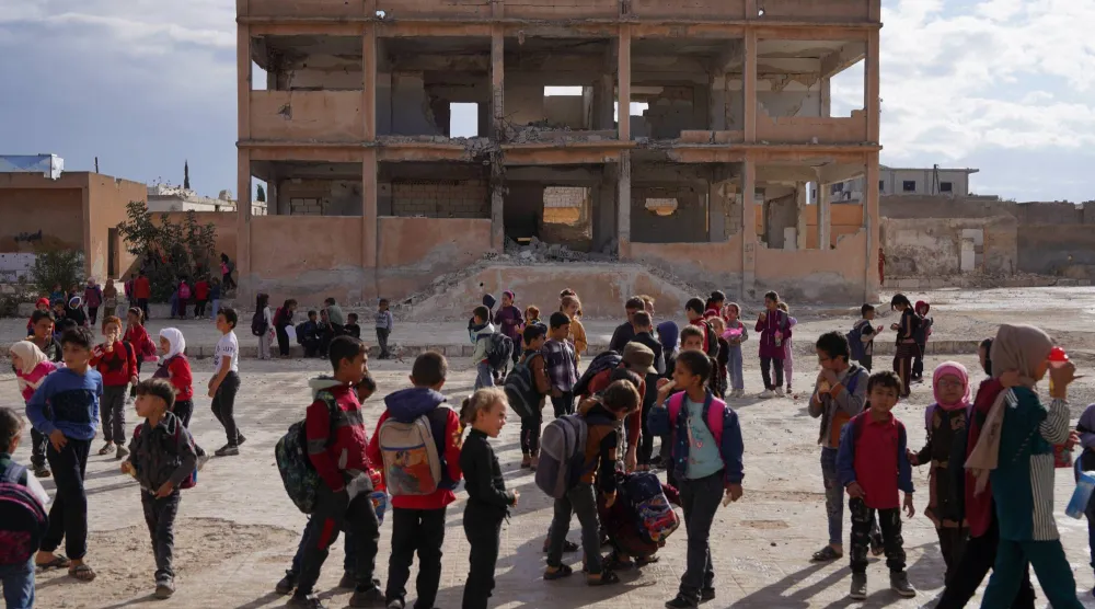 طلاب يتجمعون في ساحة مدرسة متضررة في ريف إدلب بسوريا في 9 أكتوبر 2025 (رويترز)