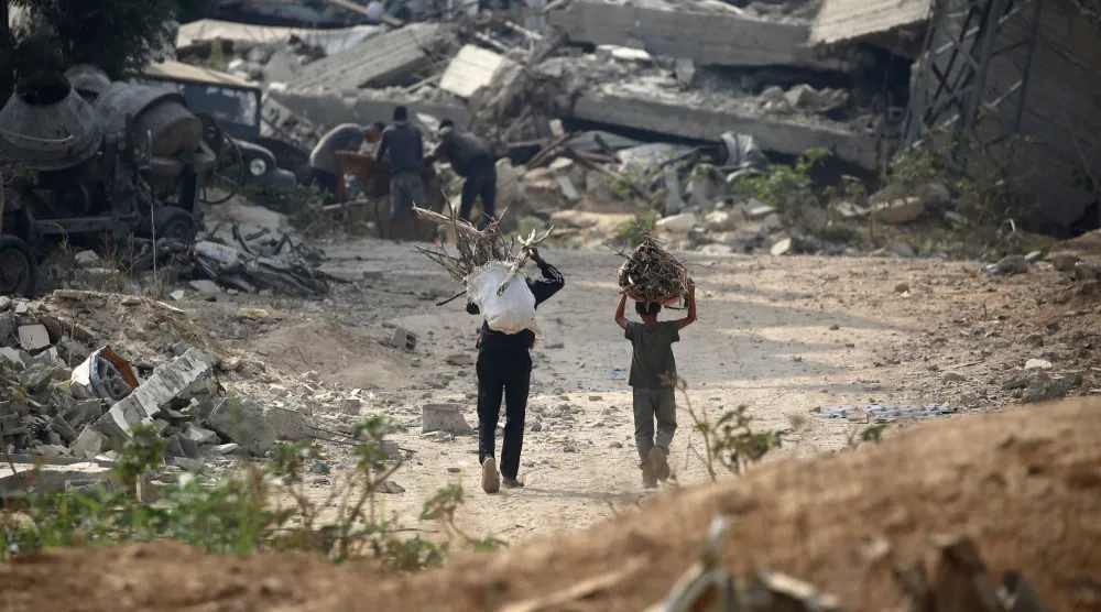 نازحان يحملان حطباً لاستخدامه وقوداً للطهي شرقي مخيم البريج للاجئين وسط قطاع غزة يوم الاثنين (أ.ف.ب)