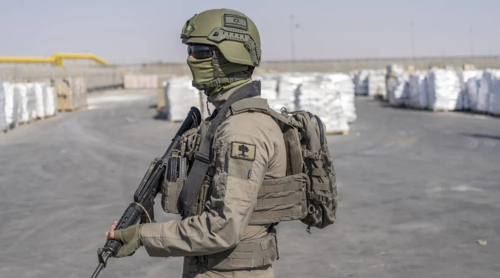 جندي إسرائيلي بجانب طرود مساعدات إنسانية تنتظر استلامها بمعبر كرم أبو سالم في قطاع غزة (د.ب.أ)