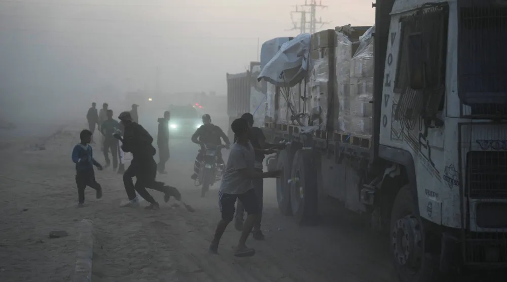 فلسطينيون يهرعون نحو شاحنات المساعدات في دير البلح بوسط غزة (أ.ب)