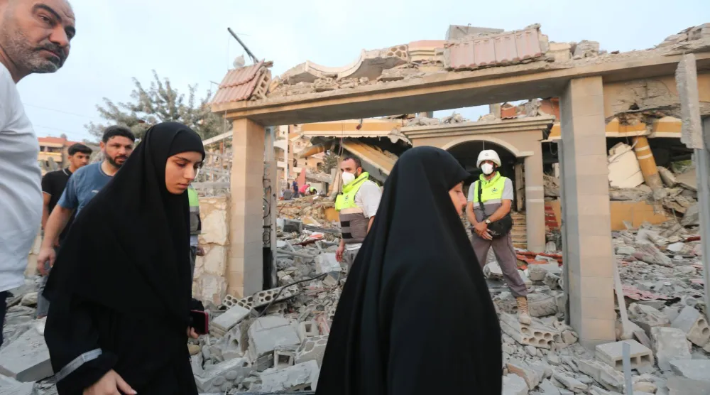 لبنانيون يسيرون قرب مبنى دمرته غارة إسرائيلية الخميس في بلدة طيردبا بجنوب لبنان (إ.ب.أ)