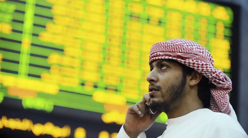 مستثمر ينظر إلى شاشة تعرض معلومات الأسهم في سوق أبوظبي للأوراق المالية (رويترز)