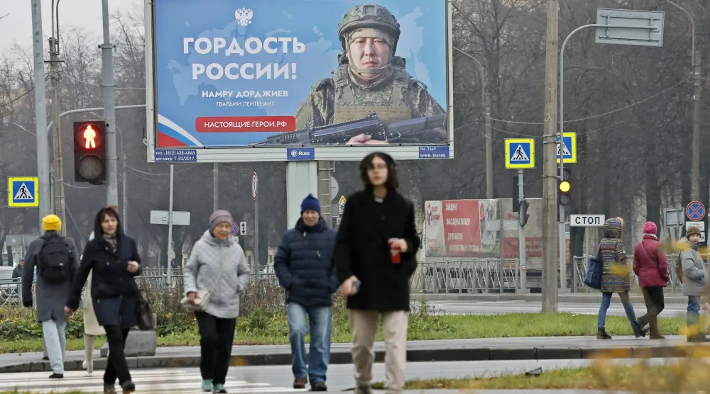 مواطنون روس يسيرون في أحد شوارع سان بطرسبورغ وخلفهم ملصق ضخم يصور جندياً مع كلام يقول: «فخر روسيا» (إ.ب.أ)