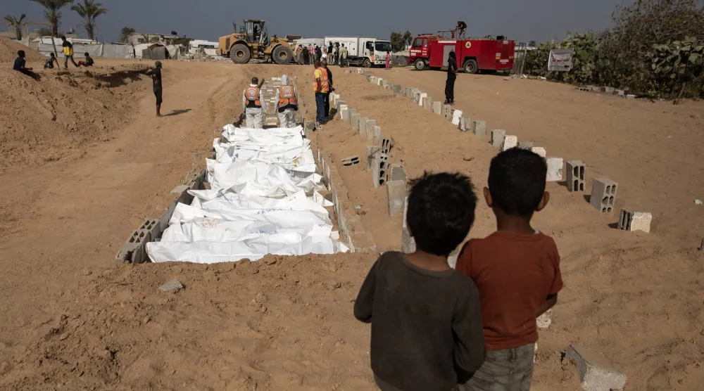 طفلان فلسطينيان يراقبان دفن جثامين فلسطينيين مجهولي الهوية أعادتهم إسرائيل في مقبرة جماعية بدير البلح وسط غزة الاثنين (إ.ب.أ)