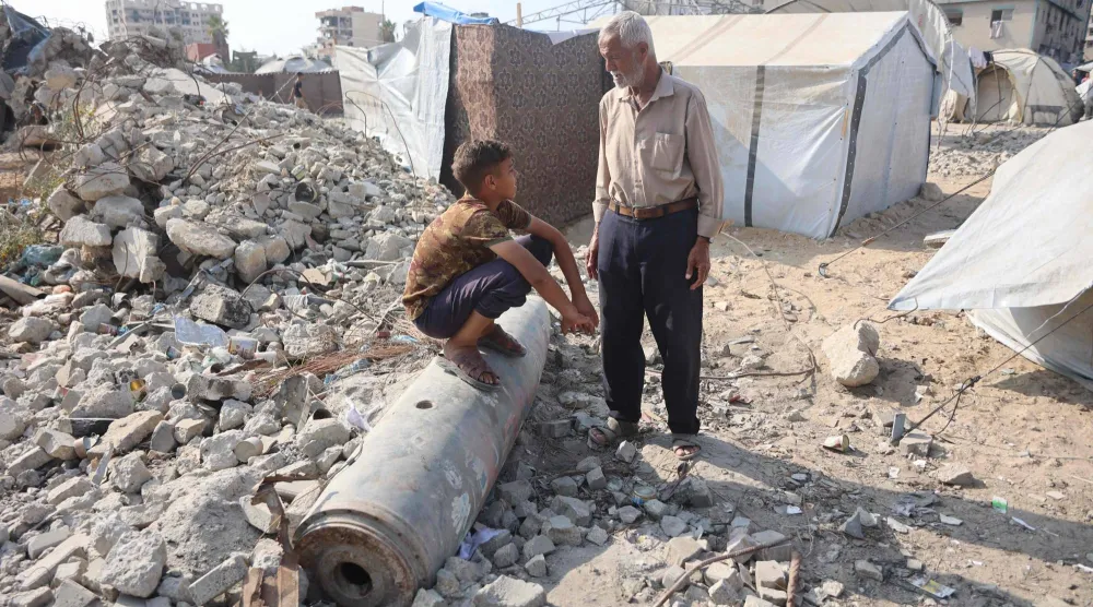 رجل فلسطيني يتحدث إلى صبي يجلس على صاروخ غير منفجر في حي الرمال بمدينة غزة يوم الأربعاء (أ.ف.ب)