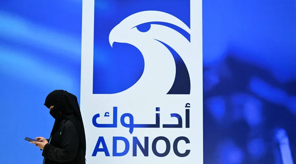 سيدة من الضيوف تنظر إلى هاتفها أثناء وقوفها في جناح شركة بترول أبوظبي الوطنية (أدنوك) خلال معرض ومؤتمر أبوظبي الدولي للبترول في أبوظبي (أ.ف.ب)