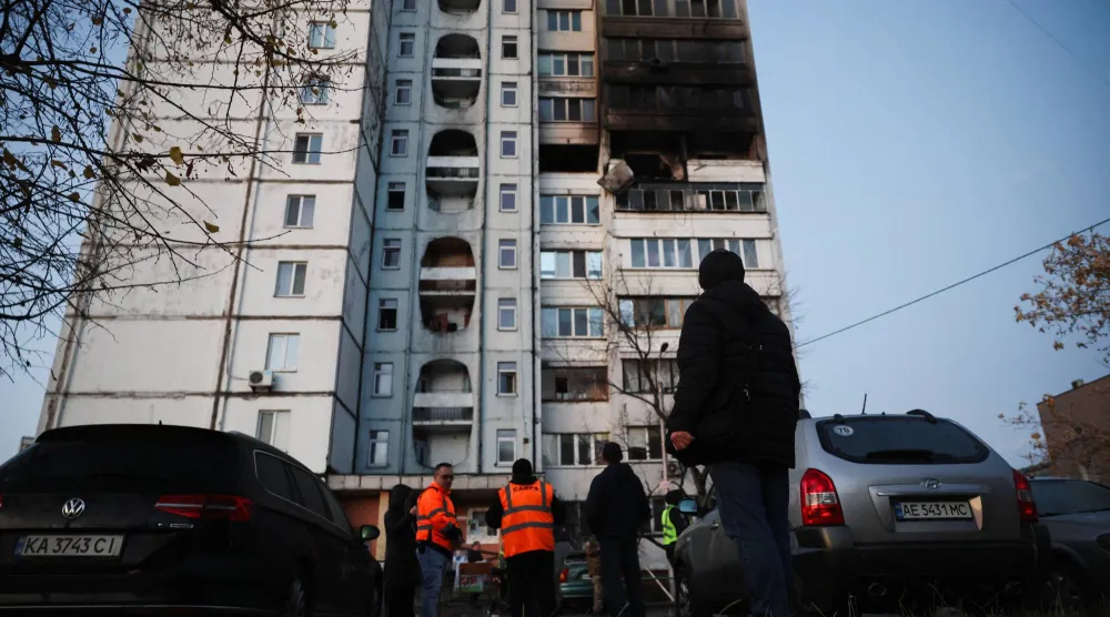 أشخاص ينظرون إلى مبنى سكني تضرر خلال غارة روسية ليلية على العاصمة الأوكرانية (رويترز)