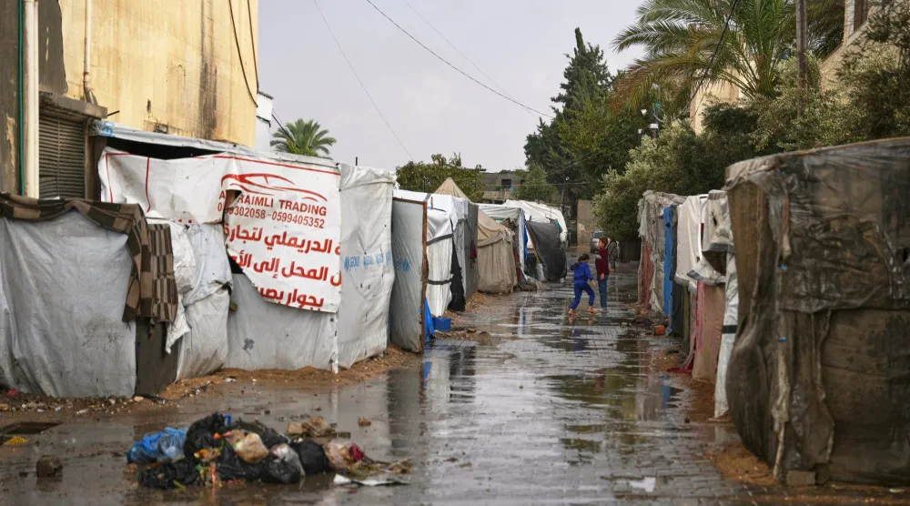 أطفال فلسطينيون يمشون بين الخيام بعد هطول الأمطار على قطاع غزة (أ.ب)