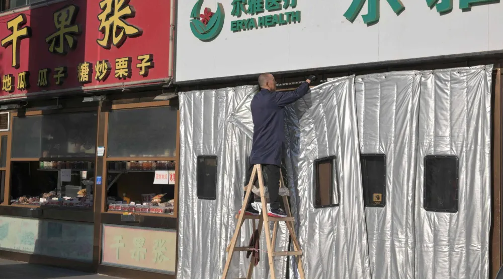 عامل يقوم بتركيب ستارة سميكة لفصل الشتاء في مجمع تجاري في بكين (أ.ف.ب)