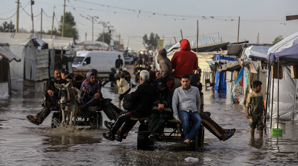 فلسطينيون يستخدمون عربات تجرها حمير لعبور شارع غمرته الأمطار في خان يونس جنوب قطاع غزة السبت (د.ب.أ)
