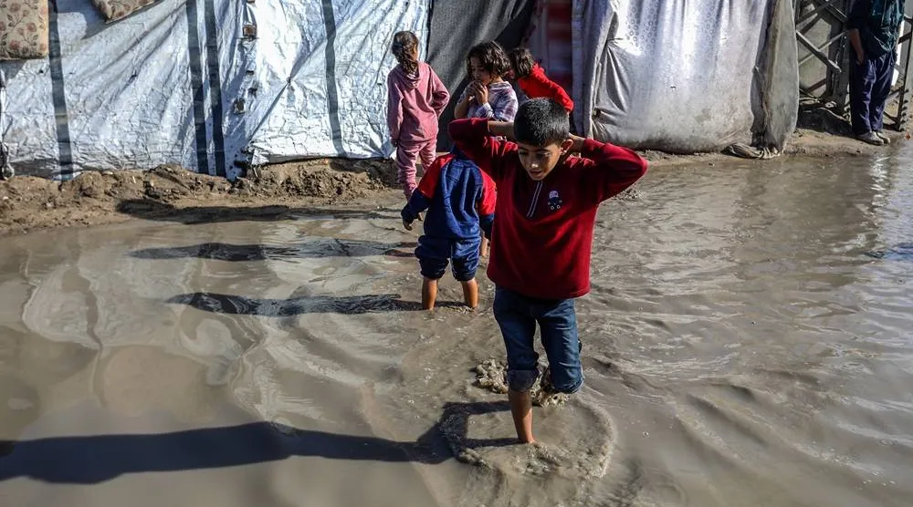 15 November 2025, Palestinian Territories, Khan Yunis: Children walk through the rainwater between their tents, as Palestinians suffer from the bitter cold and heavy rains that inundate their tents in the Al-Attar area of Mawasi, west of Khan Younis in the southern Gaza Strip. (dpa) 