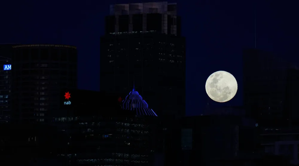 The moon rises between buildings in Sydney, Australia, Wednesday, Nov. 5, 2025. (AP Photo/Rick Rycroft)