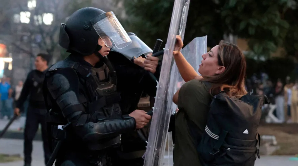 متظاهرة أمام أحد رجال الشرطة خلال اشتباكات بمسيرة ضد حكومة الرئيسة المكسيكية كلوديا شينباوم في غوادالاخارا (أ.ف.ب)