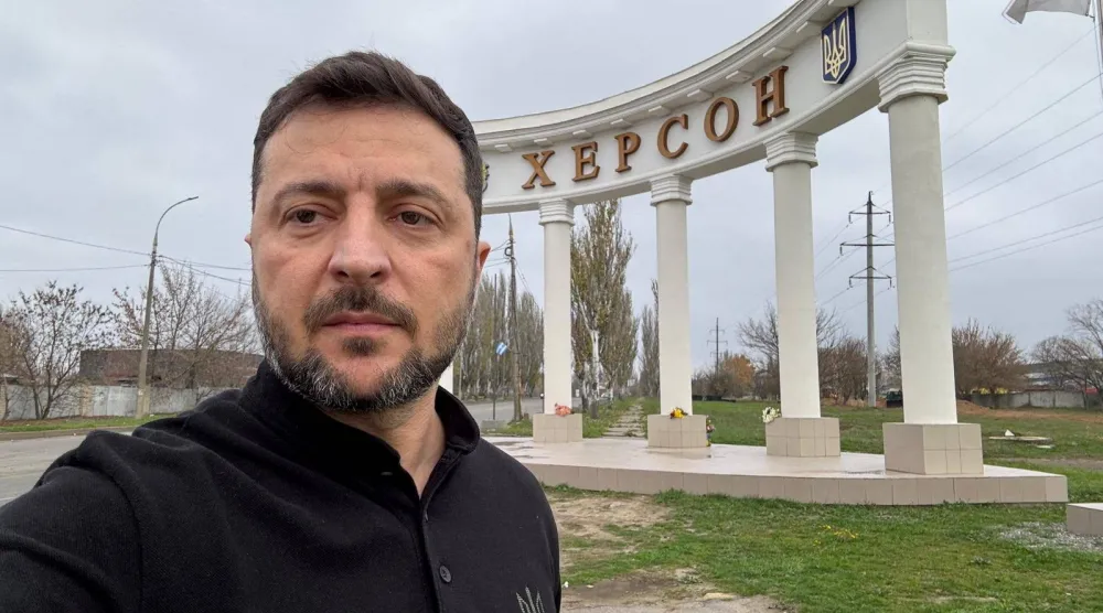 الرئيس الأوكراني فولوديمير زيلينسكي يلتقط صورة سيلفي أمام مدخل مدينة خيرسون خلال زيارته للمدينة (رويترز)