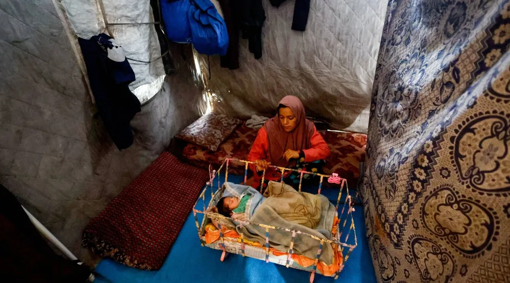 نازحة تنظر إلى طفلها داخل خيمة حاولت تحصينها من الأمطار بوسط قطاع غزة يوم الأحد (رويترز)