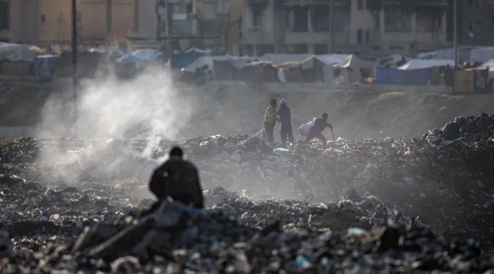 فلسطينيون يجمعون المخلفات البلاستيكية من بين أنقاض المباني في خان يونس بجنوب قطاع غزة (إ.ب.أ) 