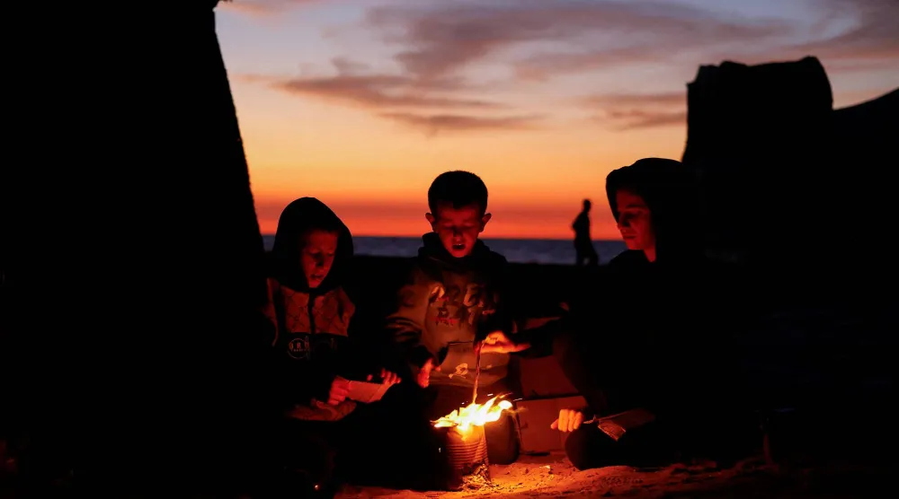أطفال فلسطينيون يجلسون بجوار النار في وسط قطاع غزة (رويترز)