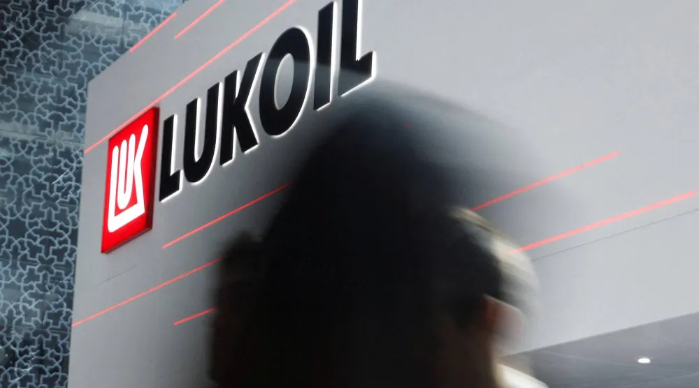 أشخاص يمرون أمام شعار شركة «لوك أويل» خلال معرض ومؤتمر أبوظبي الدولي للبترول في أبوظبي (رويترز)