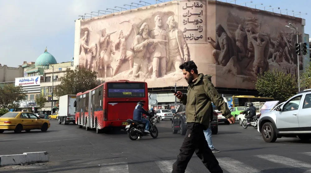 إيراني يعبر ميدان «انقلاب» وسط طهران بالقرب من لوحة إعلانية كُتب عليها بالفارسية: «ستركعون أمام إيران مرة أخرى» الاثنين (إ.ب.أ)