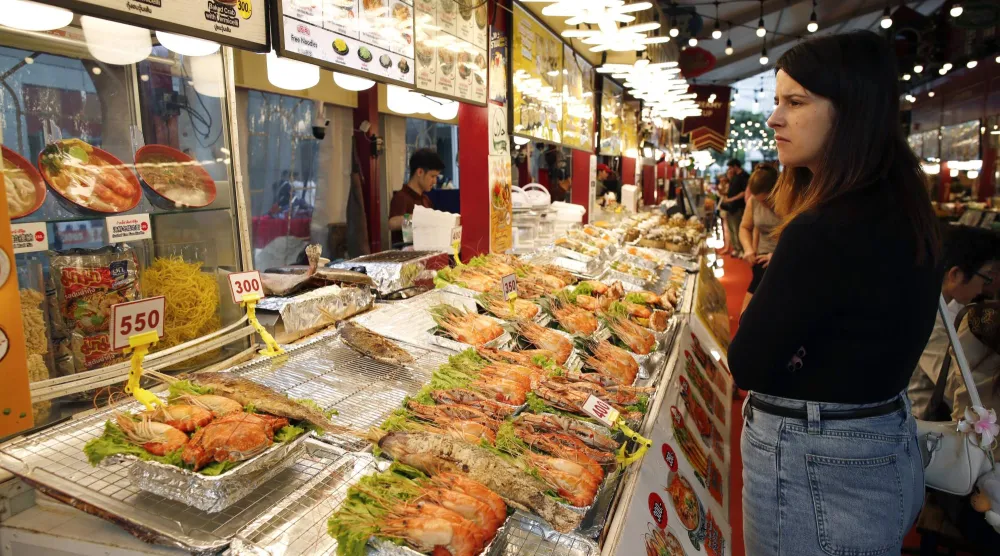 سائحة تشتري المأكولات البحرية بأحد أسواق بانكوك (إ.ب.أ)