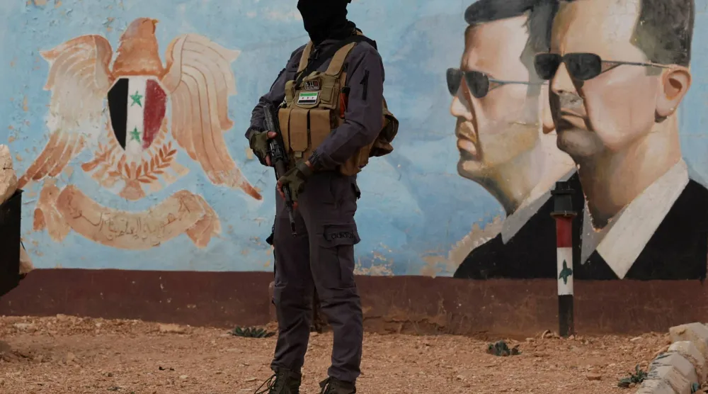 عنصر من القوات السورية الجديدة بالقرب من صورة للرئيس المخلوع بشار الأسد وشقيقه ماهر بمقر الفرقة الرابعة بدمشق (رويترز)
