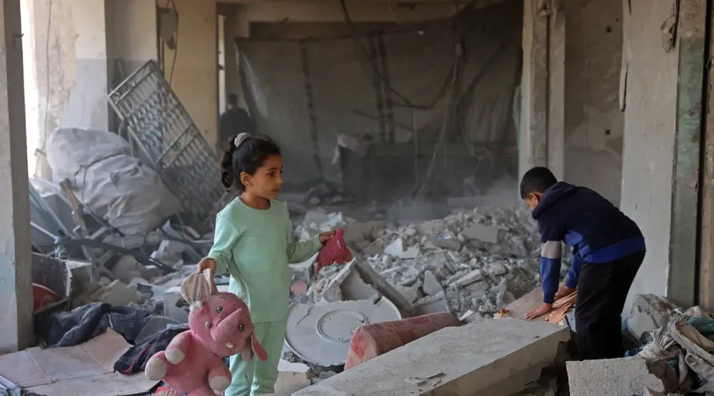 Gazze şehrinin ez-Zeytun mahallesinde yerinden edilmiş kişilerin barındığı bir binanın enkazı arasında oyuncaklarını taşıyan Filistinli bir kız çocuğu (AFP)