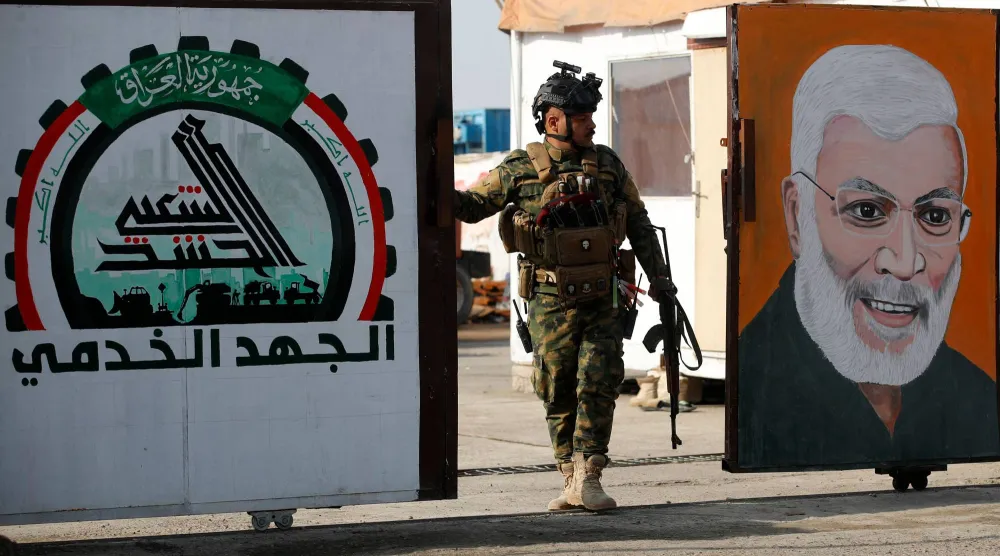 یک نیروی «الحشد الشعبی» در حال نگهبانی از دروازه‌ای در بغداد است که تصویر ابومهدی المهندس بر آن نصب شده است  (AFP)