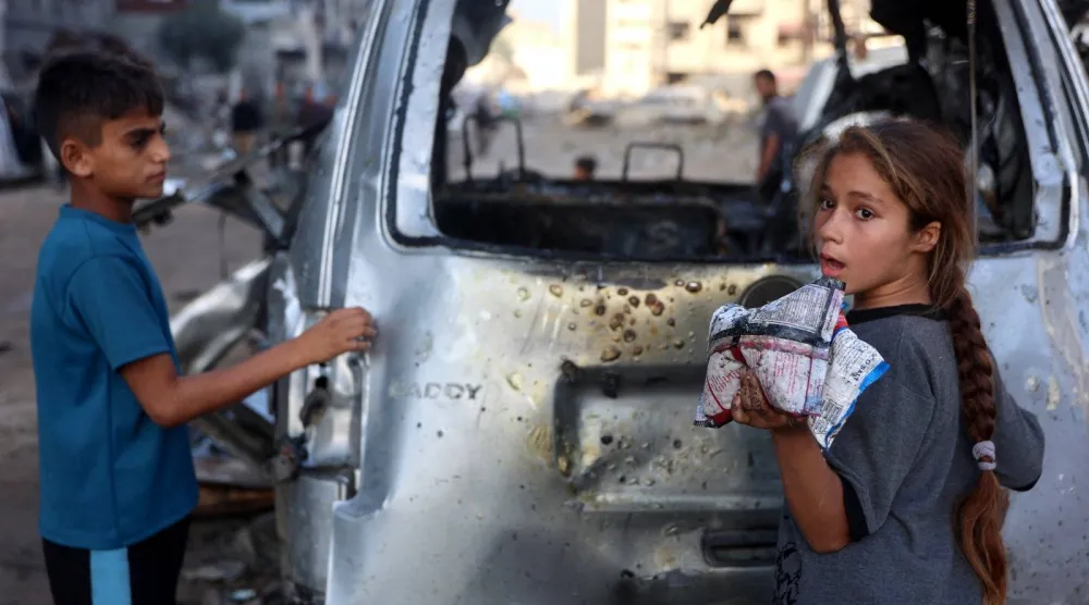 طفل وفتاة فلسطينيان ينظران إلى سيارة استهدفتها قوات الجيش الإسرائيلي في مدينة غزة (أ.ف.ب)