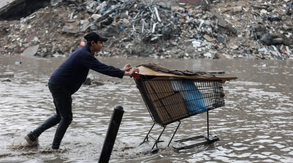 فلسطيني في مدينة غزة يوم الثلاثاء يدفع عربة وسط مياه الأمطار التي أغرقت خيام النازحين (أ.ف.ب)