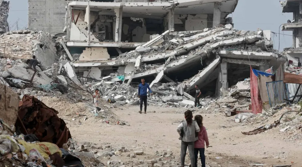 Gazze şehrinde savaşta hasar gören bir binanın önünde duran Filistinliler (AFP)