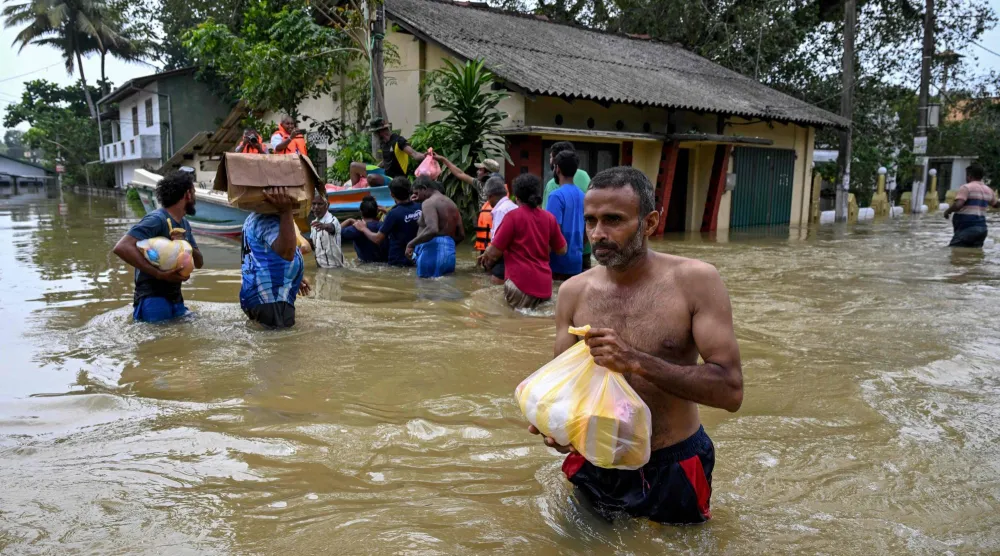 سكان يحملون أمتعتهم في منطقة غمرتها الفيضانات في سريلانكا (أ.ف.ب)
