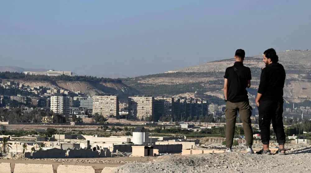 شابان سوريان يقفان على تلة في داريا مُطلّة على القصر الرئاسي الفسيح للرئيس السابق بشار الأسد في دمشق أواخر أكتوبر الماضي (أ.ف.ب)