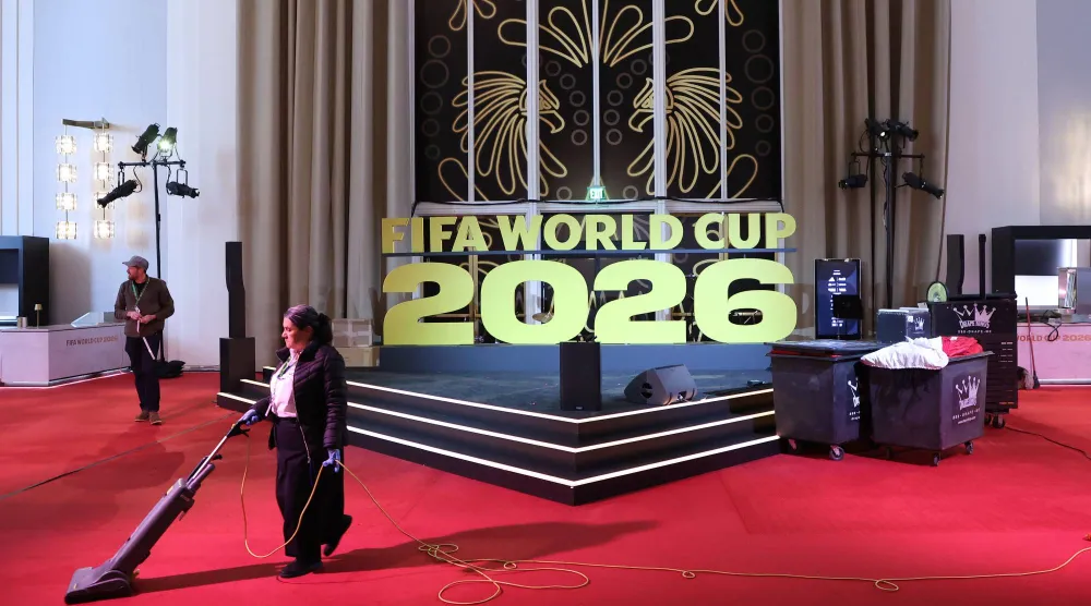 عامل نظافة ينظّف السجادة الحمراء بجوار لافتة كُتب عليها: «قرعة كأس العالم 2026» في مركز كيندي بواشنطن (د.ب.أ)